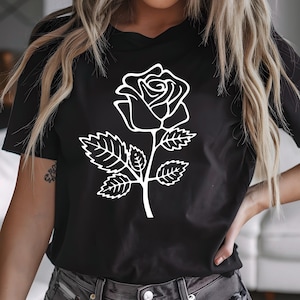 May include: Black t-shirt featuring a white outline of a rose. The rose design includes the flower, stem, and leaves. The shirt is a crew neck and has short sleeves.