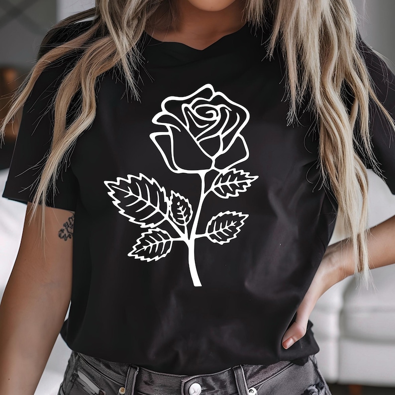 May include: Black t-shirt featuring a white outline of a rose. The rose design includes the flower, stem, and leaves. The shirt is a crew neck and has short sleeves.