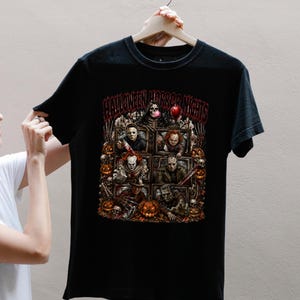 May include: A black short-sleeve t-shirt featuring a graphic print with the text HALLOWEEN HORROR NIGHTS. The design displays multiple horror movie characters inside television screens, surrounded by pumpkins, skulls, and a red balloon.