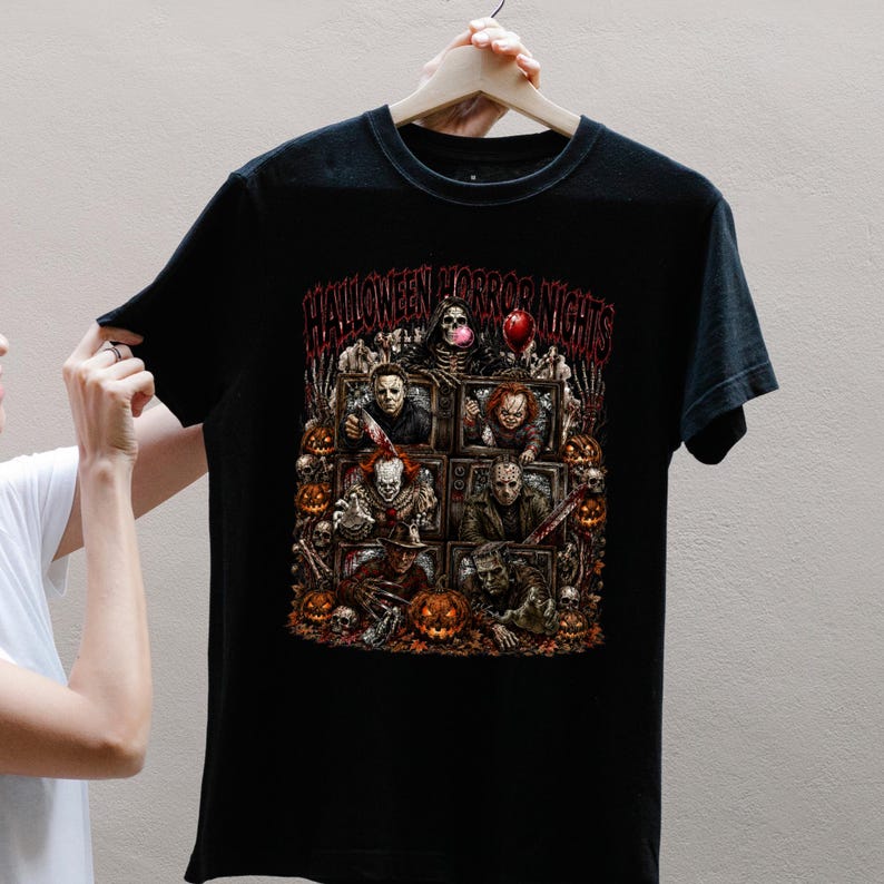 May include: A black short-sleeve t-shirt featuring a graphic print with the text HALLOWEEN HORROR NIGHTS. The design displays multiple horror movie characters inside television screens, surrounded by pumpkins, skulls, and a red balloon.