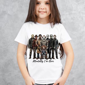 May include: A white short-sleeved t-shirt featuring a graphic print of various horror movie characters standing together, with a small doll figure sitting in front. The text "Mentally I'm Here" is printed in a black script font below the characters.