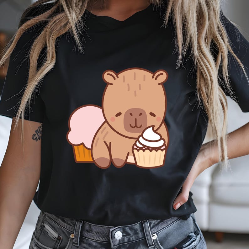 K&ouml;nnte beinhalten: Schwarzes T-Shirt mit einem Cartoon-B&auml;ren, der einen Cupcake h&auml;lt. Der B&auml;r ist hellbraun und l&auml;chelt. Ein rosa Cupcake und ein wei&szlig;er Cupcake sind ebenfalls im Bild. Das T-Shirt hat einen V-Ausschnitt.
