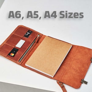 Può includere: Un taccuino in pelle marrone con chiusura a zip e una tasca per le carte. Il taccuino è aperto per rivelare una pagina vuota e un interno in pelle marrone. Il testo "A6, A5, A4 Sizes" è visibile nella parte superiore dell'immagine.