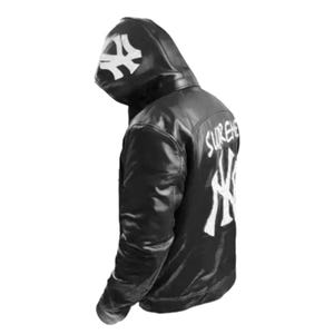 Op de afbeelding: Zwarte jas met capuchon en wit "NY" logo op de rug en capuchon. Het woord "SUPREME" staat boven het logo. De jas is gemaakt van een glanzend materiaal.