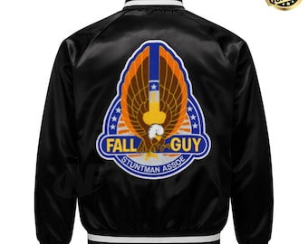 Pode incluir: Casaco bomber de cetim preto com punhos e gola listrados em branco e preto. As costas apresentam um grande patch com as palavras "FALL GUY STUNTMAN ASSOE" e um gráfico de uma águia com as asas abertas.