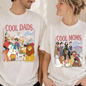 May include: Two white t-shirts with the text "COOL DADS Club" and "COOL MOMS Club" in a red and blue design. The shirts feature cartoon characters. The shirts are worn by two people.