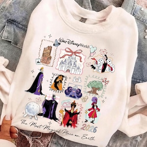 May include: White sweatshirt featuring colorful illustrations of Disney characters and landmarks. The design includes images of a castle, villains, and the text "Walt Disney World" and "The Most Magical Place on Earth 2026".