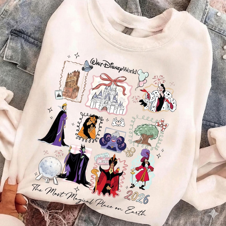 May include: White sweatshirt featuring colorful illustrations of Disney characters and landmarks. The design includes images of a castle, villains, and the text "Walt Disney World" and "The Most Magical Place on Earth 2026".