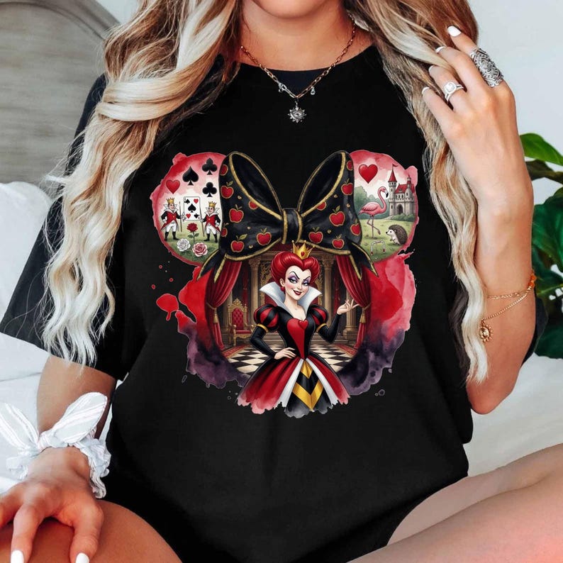 Puede incluir: Camiseta negra con un gr&aacute;fico colorido de la Reina de Corazones de Alicia en el pa&iacute;s de las maravillas. El dise&ntilde;o incluye un gran lazo con manzanas rojas, naipes, un flamenco y un castillo. La Reina lleva un vestido rojo y negro.