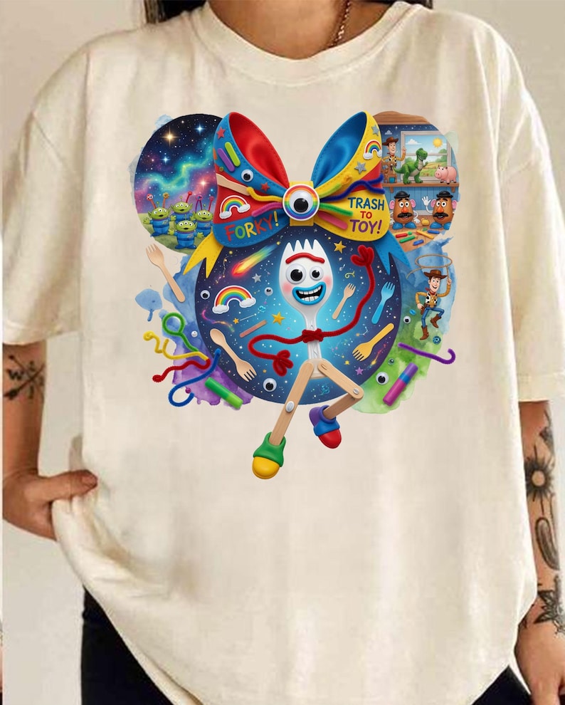 May include: Cream-colored t-shirt featuring a colorful graphic of the character Forky from the movie Toy Story 4. The design includes a bow, the words "Trash to Toy!" and other characters from the movie.