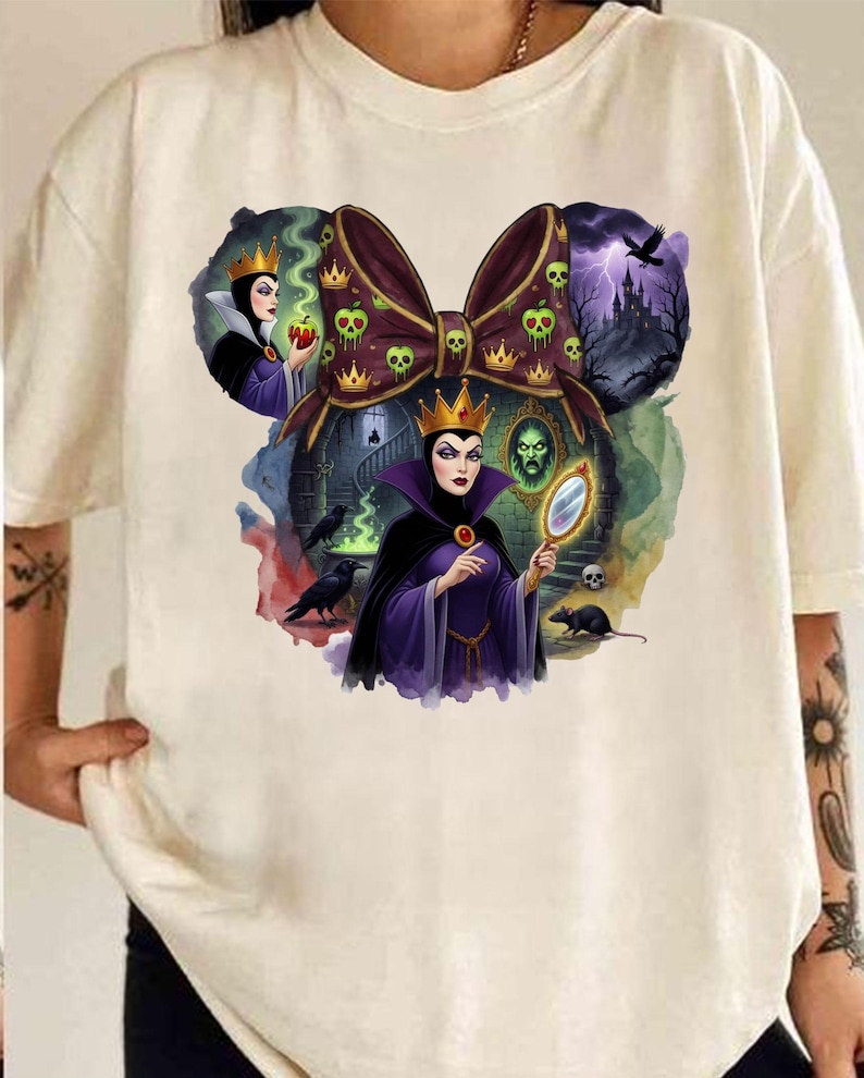 Puede incluir: Camiseta color crema con un gr&aacute;fico de un lazo con calaveras y coronas, e im&aacute;genes de una reina sosteniendo un espejo y una manzana. El dise&ntilde;o incluye un castillo, cuervos y una rata. La obra de arte es de estilo caricatura.