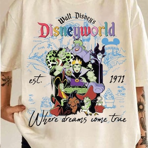 May include: Cream-coloured t-shirt with a colourful graphic of Disney villains. The design includes the text "Walt Disney's Disneyworld" and "Where dreams come true", with the year "1971". The graphic showcases various animated characters.