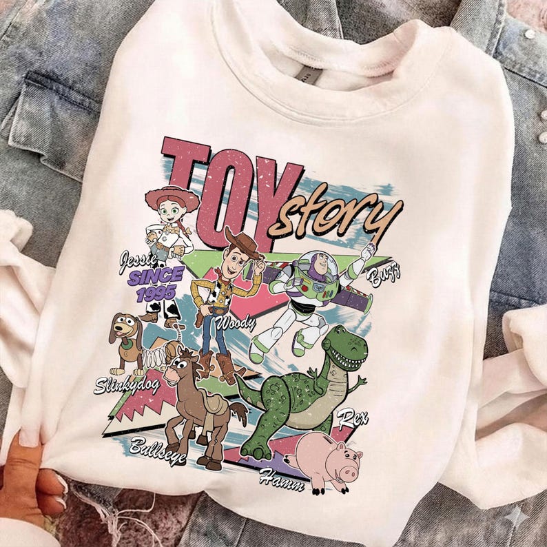 Puede incluir: Sudadera blanca de cuello redondo con un gr&aacute;fico colorido de los personajes de Toy Story, incluyendo a Woody, Buzz Lightyear y Rex. El dise&ntilde;o incluye el texto "Toy Story" y "Since 1995". La sudadera es de material suave.