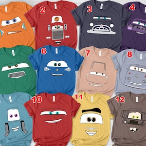 May include: A collection of twelve short-sleeved t-shirts in various colors, each featuring a cartoon car face design. Colors include orange, red, navy, purple, green, blue, tan, light blue, and yellow. The designs vary, with different car expressions.