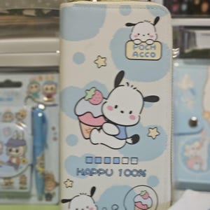 May include: A light blue and white wallet featuring a cartoon dog character with a cupcake and strawberry. The wallet has a zipper closure and the text "POCH ACCO" and "HAPPU 100%" are visible.