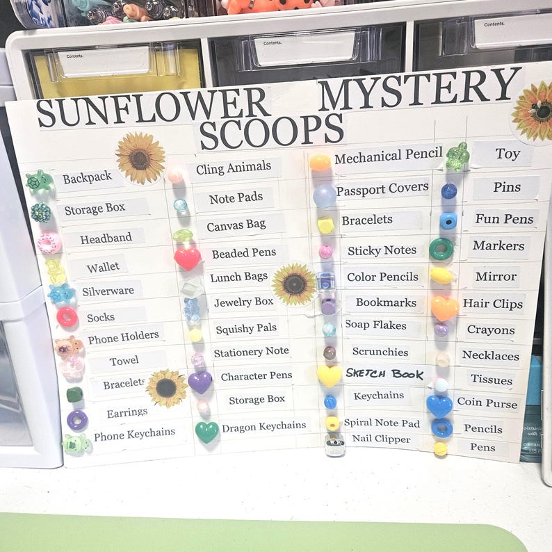May include: A white board with the words "SUNFLOWER MYSTERY SCOOPS" and a list of items like backpacks, bracelets, and keychains. The board has decorative sunflowers and colorful beads attached to it.
