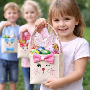 Op de afbeelding: Een kind houdt een beige paasmand met een konijnengezicht, roze stippenstrik en bloemen konijnenoren vast. De mand is gevuld met kleurrijke paaseieren en een Barbie-ei. Twee andere kinderen houden vergelijkbare manden vast.