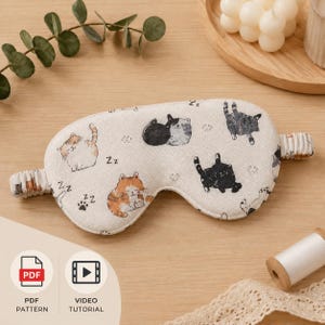Könnte beinhalten: Eine cremefarbene Schlafmaske mit einem sich wiederholenden Muster von Cartoon-Katzen in verschiedenen Posen und Farben. Die Maske hat ein elastisches Band und ist mit dem Wort "Zz" und Pfotenabdrücken verziert. Das Bild enthält auch PDF-Muster- und Video-Tutorial-Symbole.