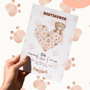 Peut inclure: Une invitation de baby shower avec un cœur floral et un ours en peluche. L'invitation comprend le texte "BABYSHOWER", la date, l'heure et l'adresse. Le fond présente un motif d'empreintes de pattes et une icône d'imprimante.