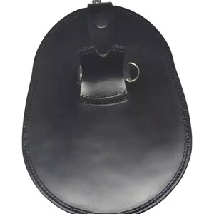 May include: A black leather sporran, a traditional Scottish accessory. The sporran has a rounded, oval shape with a flap closure and a decorative metal clasp. It features a stitched border and a strap with a metal ring.