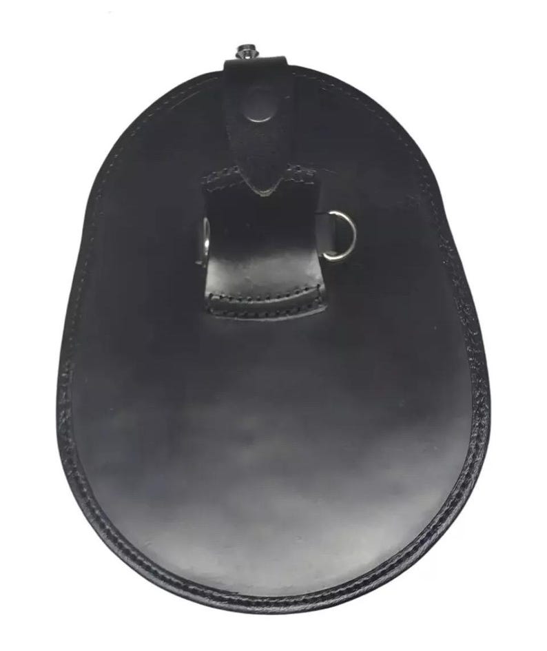 May include: A black leather sporran, a traditional Scottish accessory. The sporran has a rounded, oval shape with a flap closure and a decorative metal clasp. It features a stitched border and a strap with a metal ring.