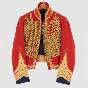 May include: A red military-style jacket with gold rope detailing and gold button accents. The jacket features gold embroidery on the sleeves and a high collar. The cuffs are navy blue. The jacket is hanging on a wooden hanger.
