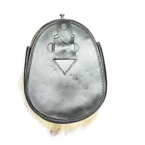 May include: A black leather sporran with a fur trim. The sporran has a flap closure with a metal button and decorative metal rings. The fur is a light tan color. The sporran is a traditional Scottish accessory.