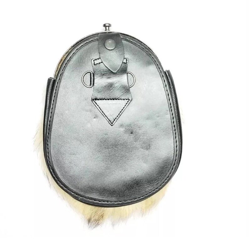 May include: A black leather sporran with a fur trim. The sporran has a flap closure with a metal button and decorative metal rings. The fur is a light tan color. The sporran is a traditional Scottish accessory.