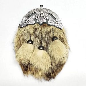 May include: A traditional Scottish sporran with a fur body in shades of brown and tan. The top features a decorative silver-toned metal cantle with thistle and Celtic knot designs. Three cream-colored tassels hang from the bottom.