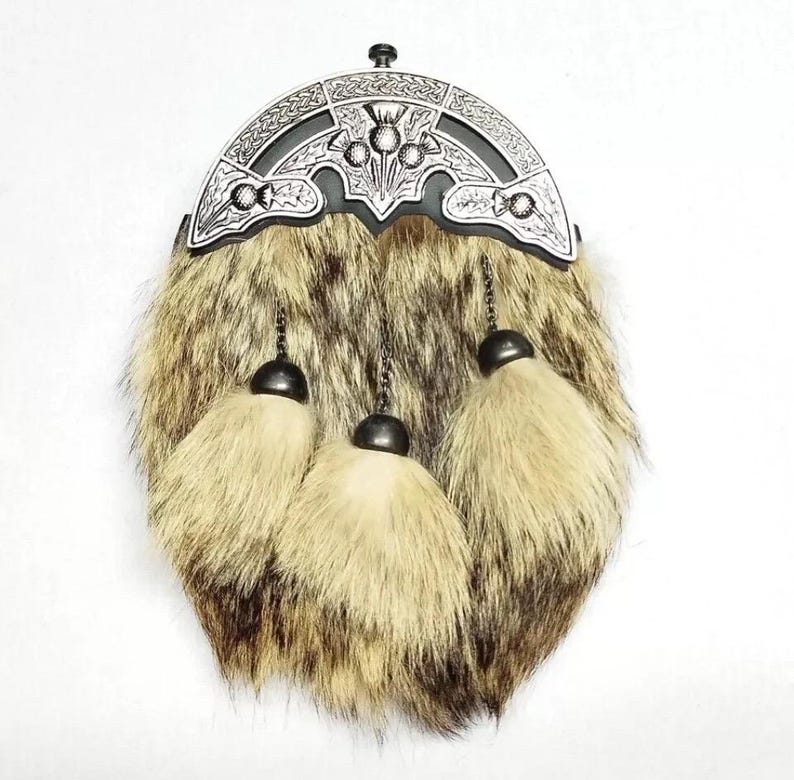 May include: A traditional Scottish sporran with a fur body in shades of brown and tan. The top features a decorative silver-toned metal cantle with thistle and Celtic knot designs. Three cream-colored tassels hang from the bottom.