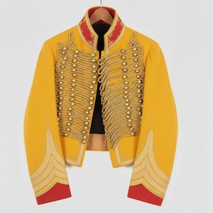 May include: A yellow military-style jacket with gold rope detailing and gold buttons. The jacket has a red collar and red cuffs. The jacket is hanging on a wooden hanger.