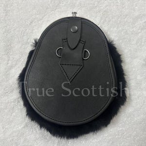 May include: Black leather sporran with a fur trim. The sporran has a flap closure with a button and two metal rings. The text "True Scottish" is visible on the front of the sporran.
