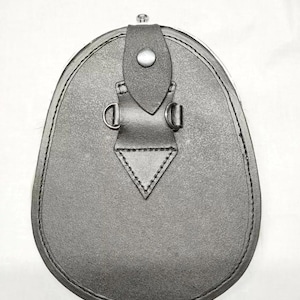 Pu&ograve; includere: Un sporran in pelle nera, una tradizionale borsa scozzese. Ha una base arrotondata e una chiusura a patta con un bottone. Lo sporran presenta cuciture decorative, anelli a D e un design triangolare nella parte inferiore.