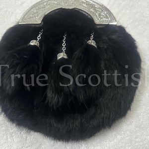 May include: A black fur sporran with a silver cantle and three decorative tassels. The text "True Scottish" is visible on the sporran. This traditional Scottish accessory is designed to be worn with a kilt.