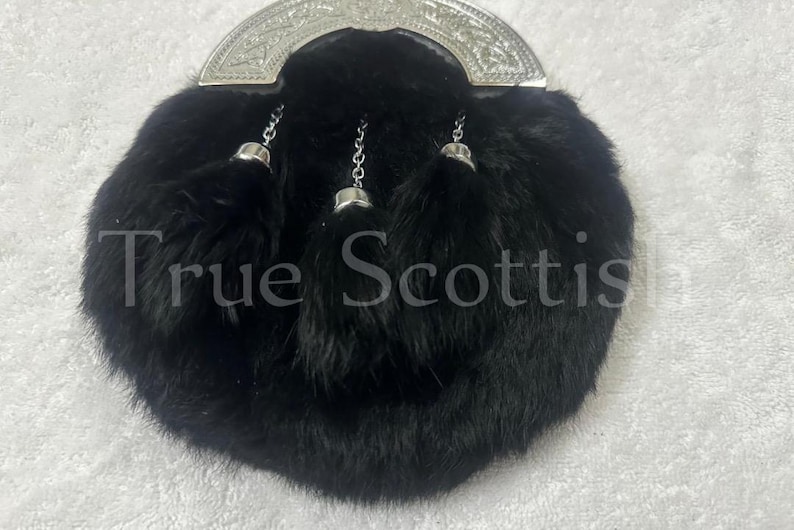 May include: A black fur sporran with a silver cantle and three decorative tassels. The text "True Scottish" is visible on the sporran. This traditional Scottish accessory is designed to be worn with a kilt.