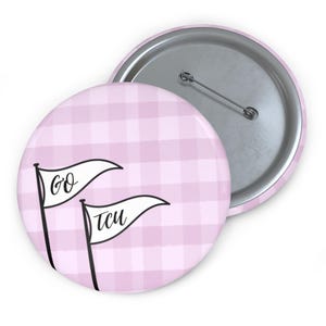 Peut inclure: Un bouton rond avec un motif vichy rose. Deux drapeaux blancs en forme de fanion avec les mots "GO" et "TCU" sont affichés sur le bouton. Le bouton a un dos en épingle métallique.