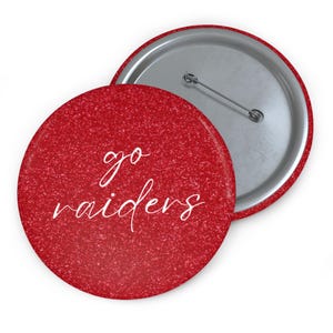 May include: A pair of round, red glitter buttons. One button is face up, displaying the white script text "go raiders". The other button is face down, showing the silver pin back.