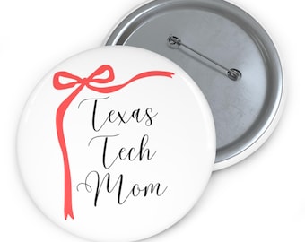 Puede incluir: Botón blanco con el texto "Texas Tech Mom" en escritura negra, acentuado por un diseño de cinta roja. El botón tiene un reverso de alfiler plateado.