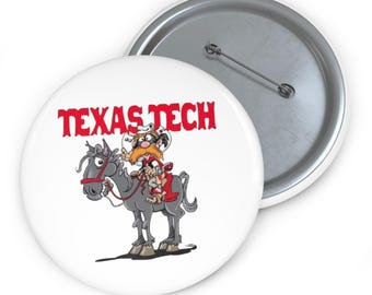 Puede incluir: Un botón blanco con una ilustración de dibujos animados de un hombre montando a caballo, con las palabras "TEXAS TECH" en rojo. El botón tiene un alfiler de metal en la parte posterior.