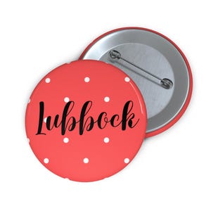 May include: A red button with white polka dots and the word "Lubbock" in black script. The button has a metal pin back. The design is simple and eye-catching, perfect for a souvenir or a statement piece.