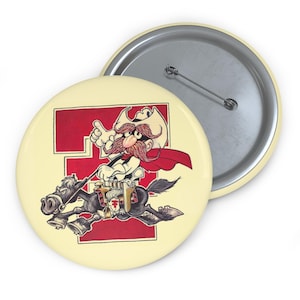 May include: A round button with a cartoon image of a cowboy riding a horse. The cowboy has a large red mustache and is wearing a white hat and red cape. The background is cream-colored with a red letter "T".