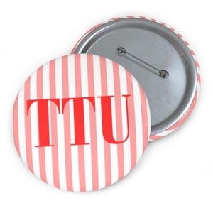 May include: Two round buttons with a red and white striped design. The text "TTU" is in red block letters on the front of the button. The back of the button is silver with a pin.