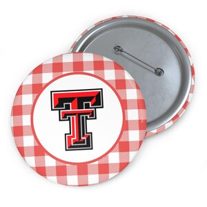 May include: Two round buttons. One button features a red and white gingham pattern around the edge. The center of the button has a white circle with a black, red, and white letter "T". The second button is visible on the right side.