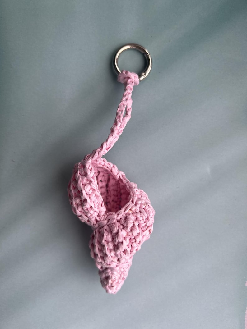 Puede incluir: Un llavero de ganchillo rosa hecho a mano con forma de zapatilla de ballet. La zapatilla est&aacute; unida a un anillo de metal plateado mediante un cord&oacute;n rosa trenzado. El llavero est&aacute; hecho de un hilo suave y texturizado.