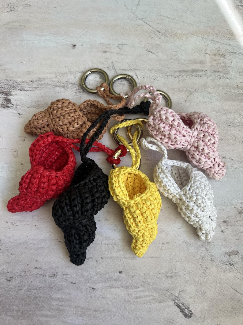 Puede incluir: Un conjunto de llaveros artesanales con forma de concha marina en varios colores: rojo, negro, amarillo y blanco. Cada llavero est&aacute; hecho de material tejido y tiene un cierre plateado para sujetarlo a llaves o bolsos.