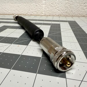 May include: A silver coaxial cable connector with a black rubber sleeve. The connector has a gold-plated center pin.