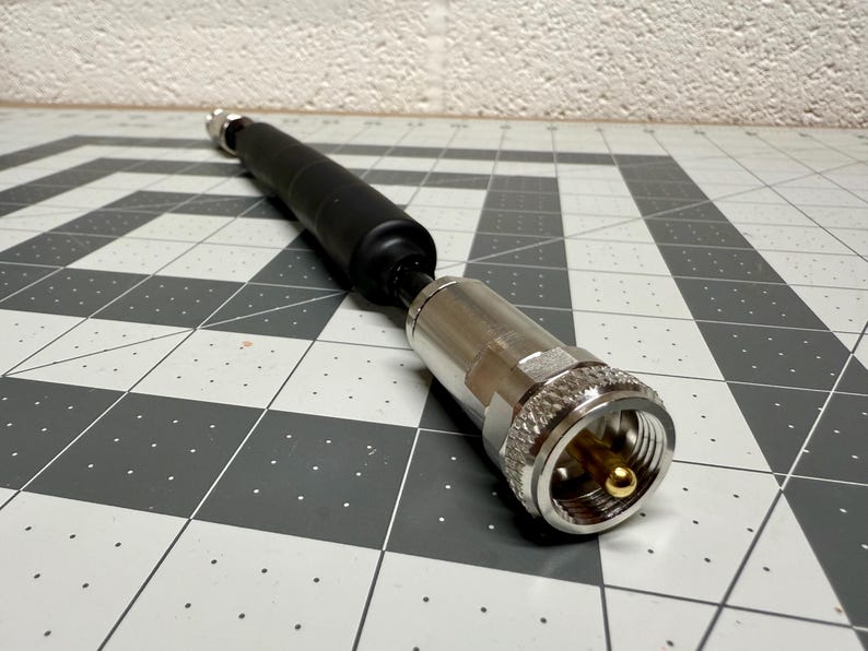 May include: A silver coaxial cable connector with a black rubber sleeve. The connector has a gold-plated center pin.