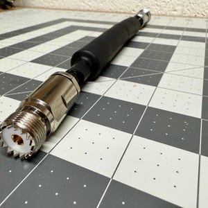 May include: A silver and black coaxial cable connector with a threaded end and a black rubber sleeve.