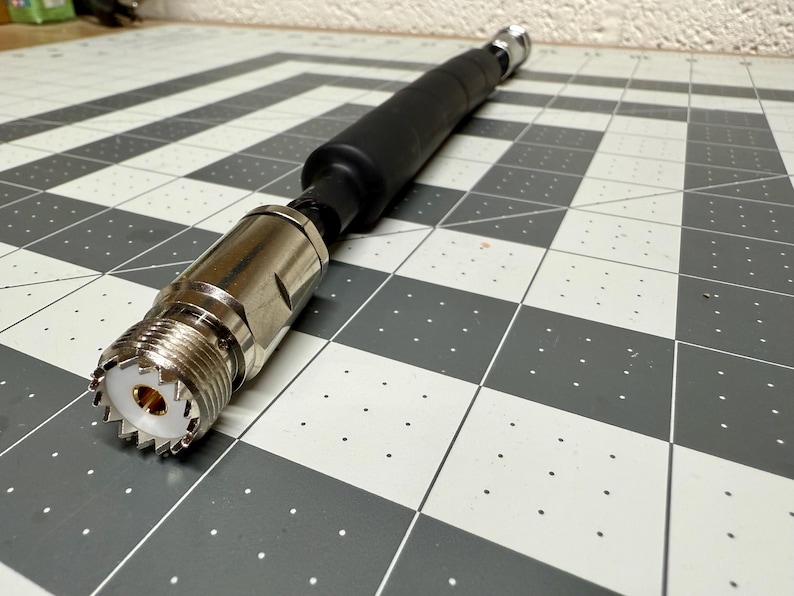 May include: A silver and black coaxial cable connector with a threaded end and a black rubber sleeve.