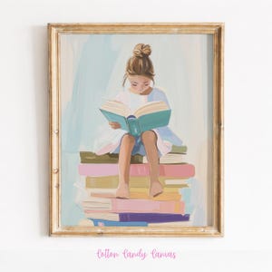 May include: A framed art print depicts a young person engrossed in a book, seated atop a stack of colorful books. The artwork features soft pastel colors, with a gold-colored frame. The text "Cotton Candy Canvas" is at the bottom.